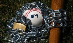Brownsburg, IN - December 2: An Official Rawlings Major League Baseball sits with a bat, lock and chain to represent the lockout between Major League Baseball (MLB) and the Major League Baseball Players Association (MLBPA) on December 2, 2021 in Brownsburg, IN. (Photo by James Black/Icon Sportswire via Getty Images)